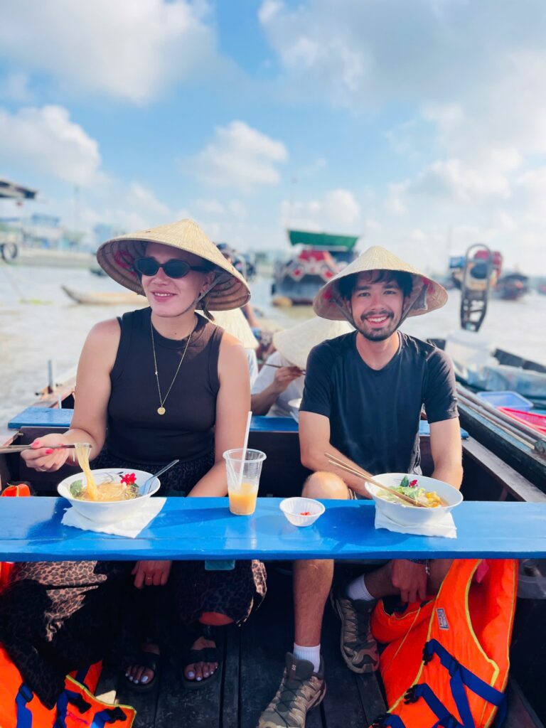 Travelers enjoying traditional Vietnamese breakfast on a boat at Cai Rang Floating Market.